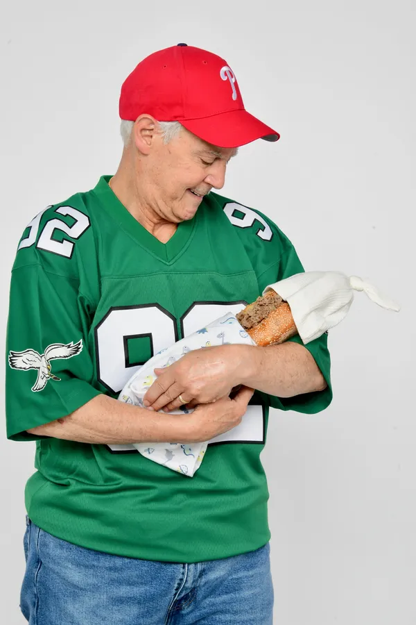 Nick Colletta in an Eagles jersey cradling a cheesesteak like a newborn